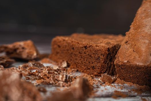 Close up of a Chocolate brownies on a rustic wooden table with chocolate chips and chocolate soil next to the brownie portions.