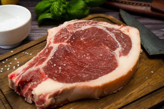 A bone-in steak or t-bone or porterhouse raw on a cutting board on a wooden table. High view. Close-up.