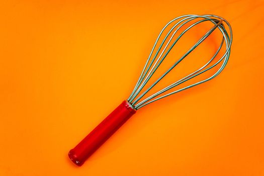 Metal rod whisk with wooden handle insulated on orange background. Kitchen utensils.