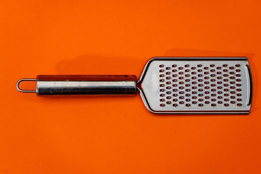Metal grater with a metal handle on a orange background. Isolated object
