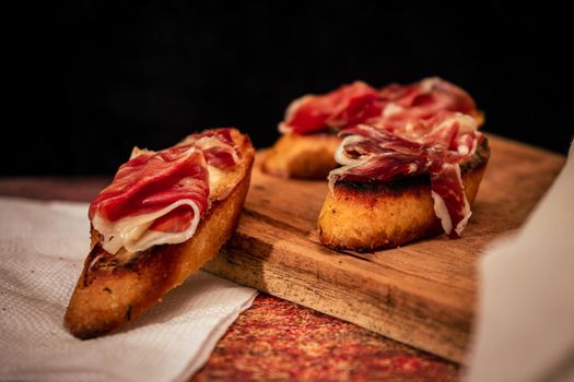 Classic Spanish tapa or brusqueta of Serrano ham with philadelphia cheese on a slice of toasted bread. Mediterranean food concept. High view