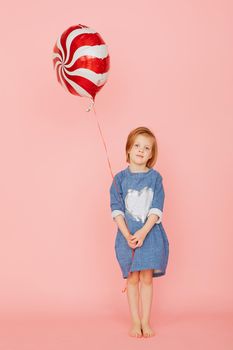 Portrait of an excited pretty little girl celebrating birthday and holding balloon in hand on over pink background