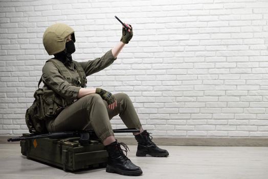 soldier girl in a helmet is sitting and talking on a mobile phone