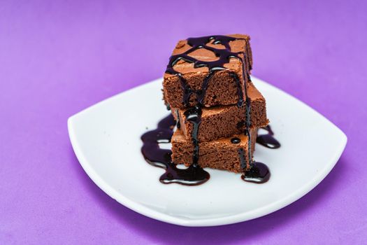 Stack of chocolate brownies on a white plate with purple background. High view.