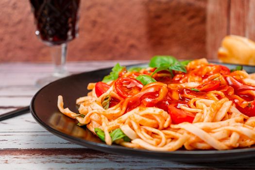 Spaghetti pasta with an exquisite homemade tomato sauce with homemade basil leaves served on a black plate on a rustic table. High view.