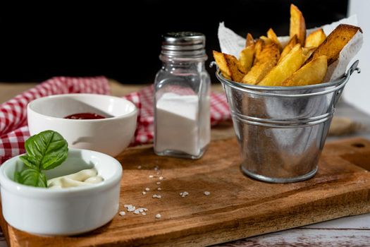French fries in a metal pot with aioli and ketchup on a wooden board. copy space