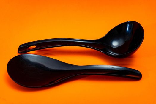 Set of kitchen spoon and spatula in black plastic isolated on orange background.