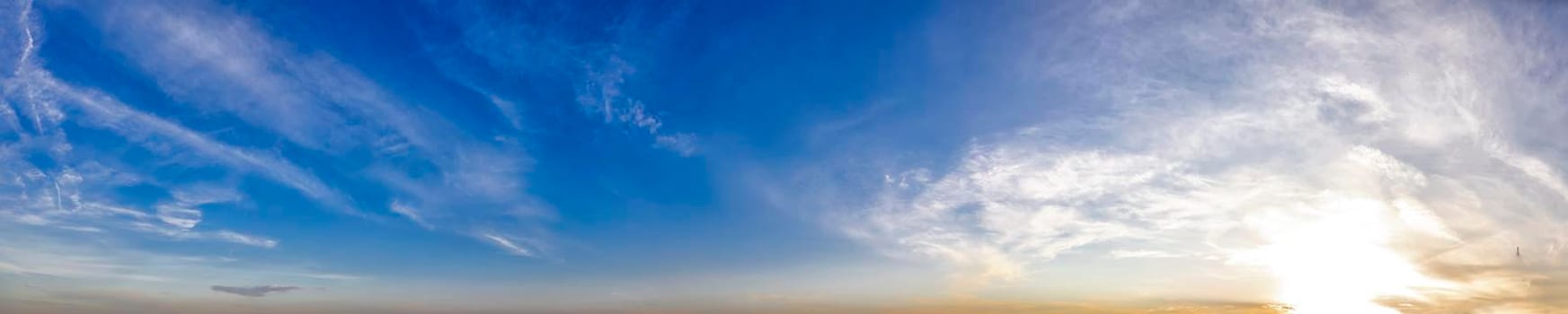Panoramic view of blue sky with clouds and sun.