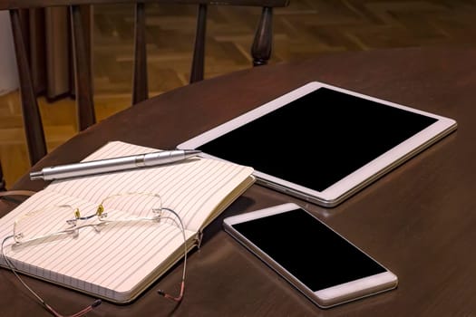 Office table: mobile phone, tablet, glasses, notebook and pen with copy space. Gadgets on a wooden table.  