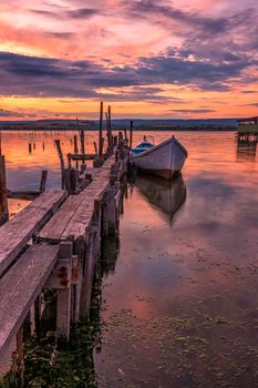 Amazing mood sunset at a lake coast with a boat at a wooden pier. Vertical view