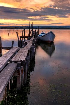 Amazing mood sunset at a lake coast with a boat at a wooden pier. Vertical view