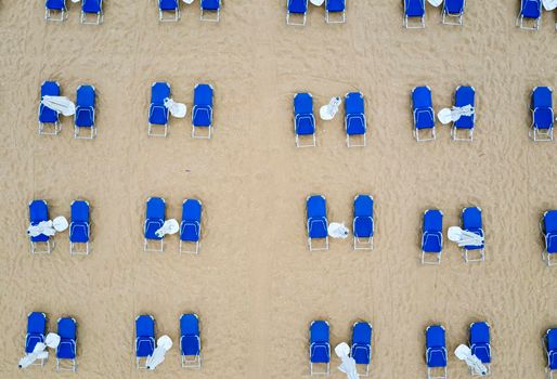 Aerial top view of a beach with white umbrellas and blue lounge chairs