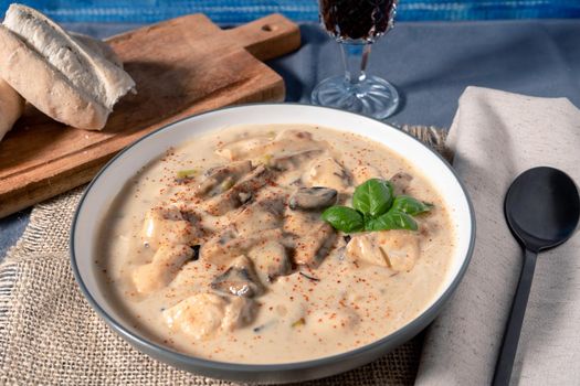 A Homemade cream of chicken and mushroom soup or French style chicken fricassee, in a soup bowl on a wooden table. High view.