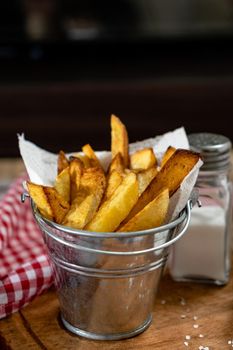 French fries in a metal pot with aioli and ketchup on a wooden board. Vertical orientation, copy-space.