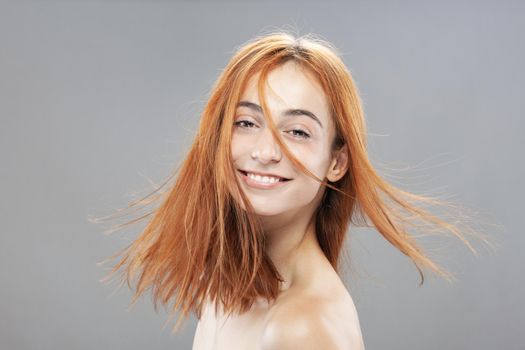 Beautiful dark burnt orange windy hair girl smiling. Studio portrait with happy face expression against gray background.