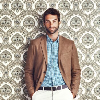 Portrait of a stylishly dressed young man posing against a wallpaper background.