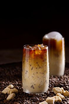 Tasty Iced coffee. Tasty ice coffee with milk, cold drink in glass with ice on dark coffee background Copy space.