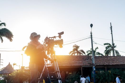 Unrecognizable cameraman films a live TV show in a park outdoors at sunset