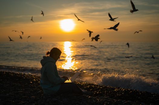 Caucasian woman typing on a laptop on the seashore at sunset. Freelance work