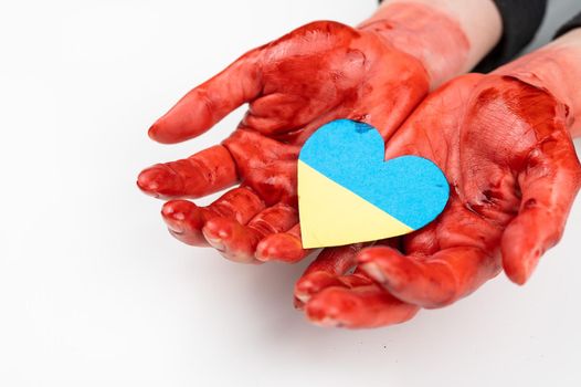 Woman with hands covered in blood holding a heart with the flag of ukraine on a white background