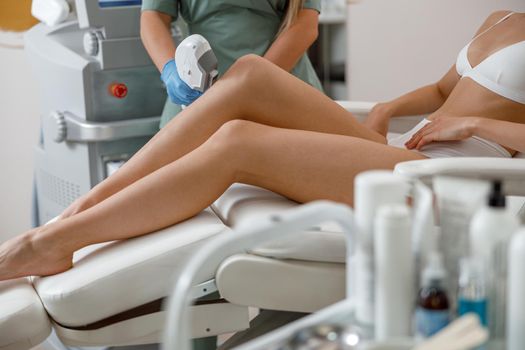 Photo epilation hair removal process on legs in beauty center. Woman in underwear sitting on daybed