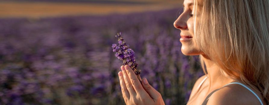 Beautiful blonde is in the field of lavender, holds a bouquet of flowers and enjoys aromatherapy. The girl's eyes are closed. The concept of aromatherapy, lavender oil, photo shoot in lavender.