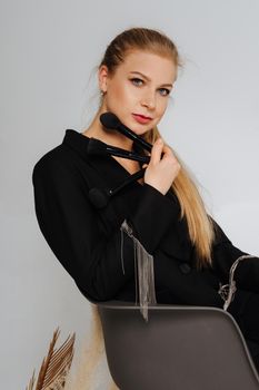 Beautiful middle aged woman makeup waving one makeup brush, winking at the camera and smiling. Blond hair and a black jacket on a light background