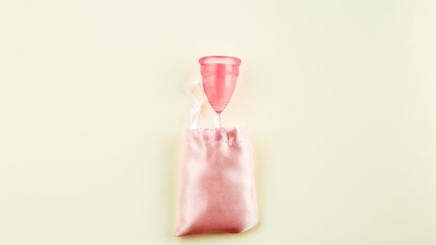 Pink Silicone Menstrual Cup and pink Storage Cloth Bag over beige Background. Space for Text, Top View. Women Sanitary Tool for Comfortable and Sustainable Periods
