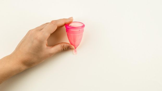 Woman hand holding a pink menstrual cup over beige background with copy space