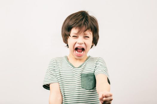 Angry kid shouting and rising his fist. Aggressive little boy with mouth wide open looking to the camera. ADHD syndrome