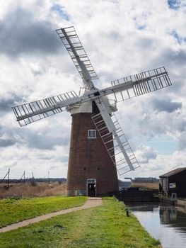 The sails of Horsey Windpump set in The Broads against a blue sky with white clouds, near Great, Yarmouth, Norfolk, UK