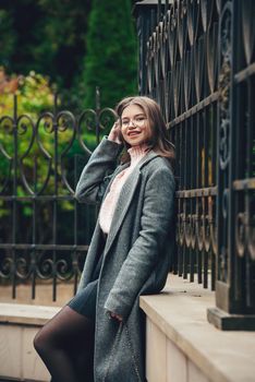 young beautiful girl posing on the street. Dressed in a stylish gray coat, knitted pink sweater and skirt. small stylish handbag