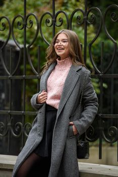 young beautiful girl posing on the street. Dressed in a stylish gray coat, knitted pink sweater and skirt. small stylish handbag