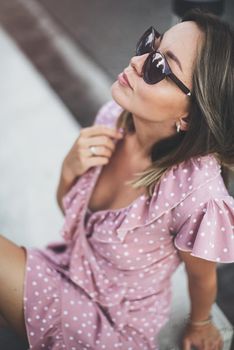 young beautiful brunette posing on the street in a pink sundress