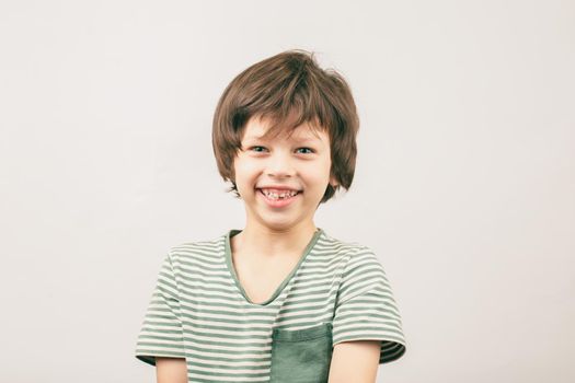 Happy six year old Caucasian boy portrait over grey background. White European kid widely smiling and looking into the camera