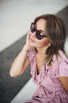 young beautiful brunette posing on the street in a pink sundress