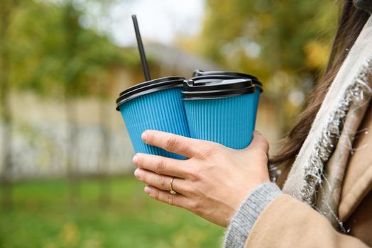 Close-up a woman hands holding three blue paper cups of coffee on autumn nature background with colorful grass.