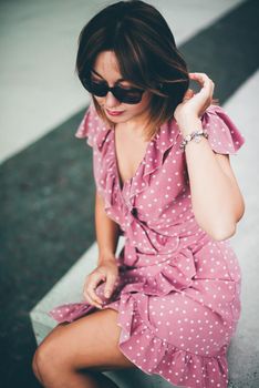 young beautiful brunette posing on the street in a pink sundress