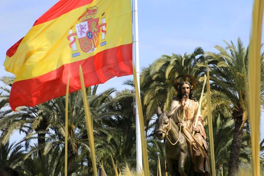 Elche, Alicante, Spain- April 10, 2022: Jesus Christ next to the Spanish flag at the traditional procession of white palms on the Palm Sunday of Elche