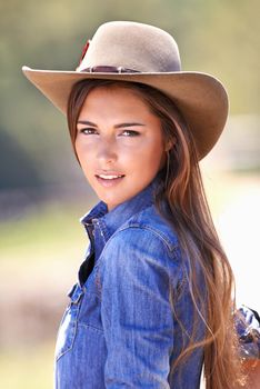 Portrait of an attractive young cowgirl standing in the sun.