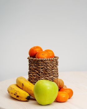 A variety of fruits and nuts on a wooden table. Tangerines in a wicker basket, bananas, apples and walnuts. photo