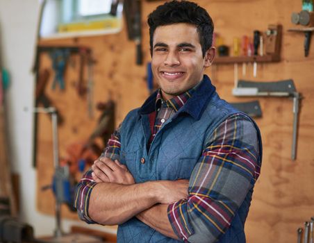 Portrait of a happy handyman standing in his workshop with his arms folded.
