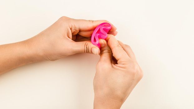 Female hand holding a pink Menstrual Cup folded with a E-Fold Method. Folding Menstrual Cup is for comfortable inserting it into vagina to collect blood during woman periods