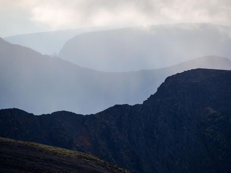 Mountain peaks in the clouds. A chain of gray mountains in the backlight. Khibiny. photo