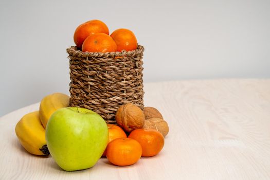 A variety of fruits and nuts on a wooden table. Tangerines in a wicker basket, bananas, apples and walnuts. photo
