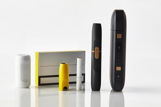 One pack, new generation black electronic cigarette, yellow cap, battery, cleaner, one heatstick isolated on white. Heating tobacco system. Hybrid between analog and electronic. Close up, copy space