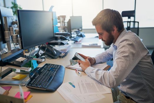 Shot of a focused young businessman texting on his cellphone while being seated behind his desk in the office.