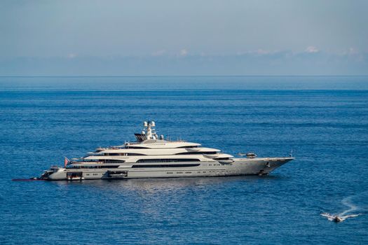 The huge mega yacht is moored in sea off the coast of the azur coastline at sunny day, the chrome plated handrail, sun reflection on glossy board of the motor boat. High quality photo