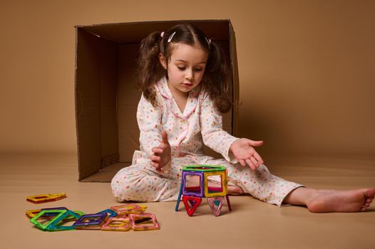 Concentrated beautiful Caucasian preschooler girl plays with lots of colorful plastic blocks constructor and building house. Fine motor skills development, kids entertainment and education concept