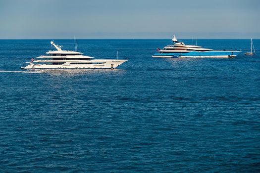 The two huge mega yachts are moored in sea at sunny day, the chrome plated handrail, sun reflection on glossy board of the motor boat. High quality photo
